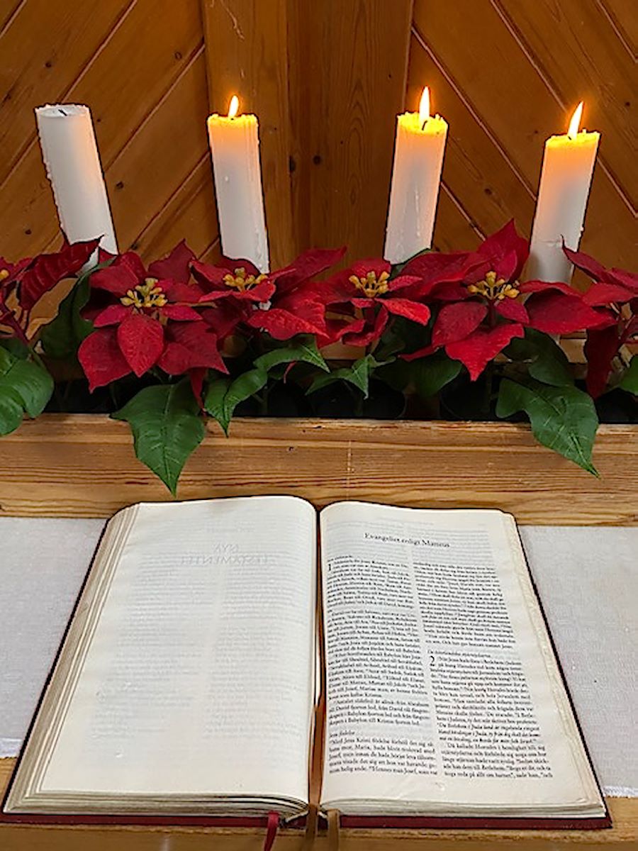 Nattvardsbord med bibel och tre tända adventsljus i adventsljusstake med fyra ljus och julblommor, Equmeniakyrkan Hallunda [foto: Carlota "Carro" Bocio Duff]