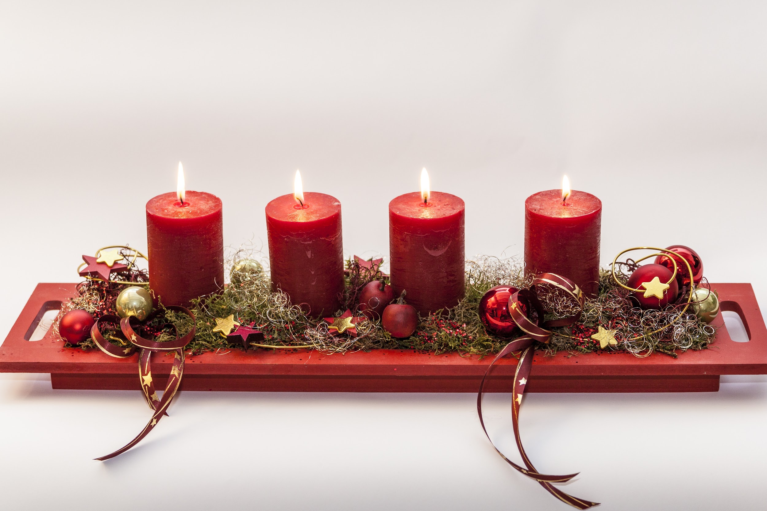 4 röda tända blockljus på röd bricka med mossa, julgranskulor, rött-guld snöre med mera dekoration.